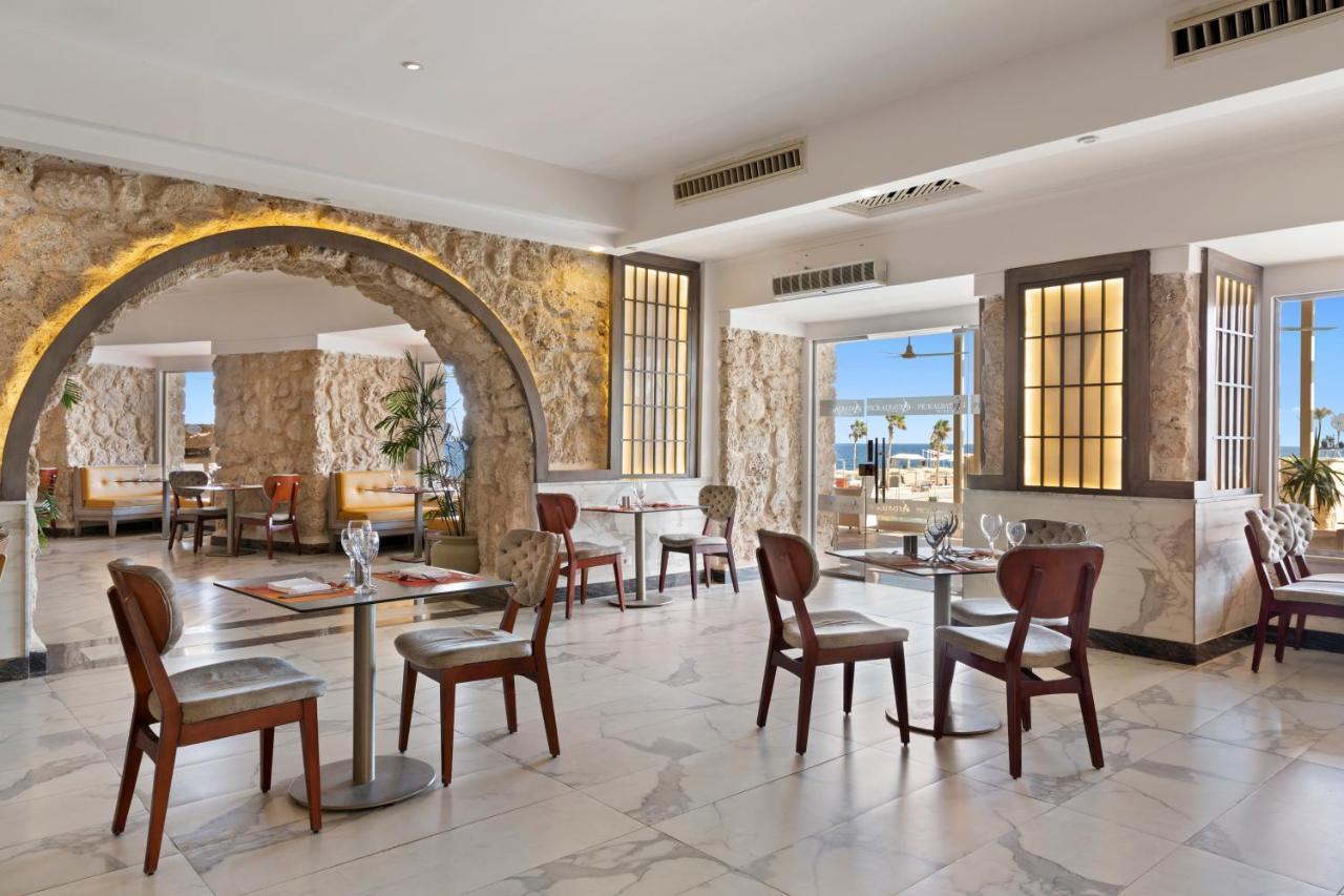 Pickalbatros Citadel Resort Sahl Hasheesh (Adults Only) Hurghada Exterior foto The photo shows a stylish and modern restaurant interior. It features a spacious layout with several tables and chairs arranged neatly. The decor includes a decorative archway and elegant wall designs, enhancing the ambiance. Large windows allow natu