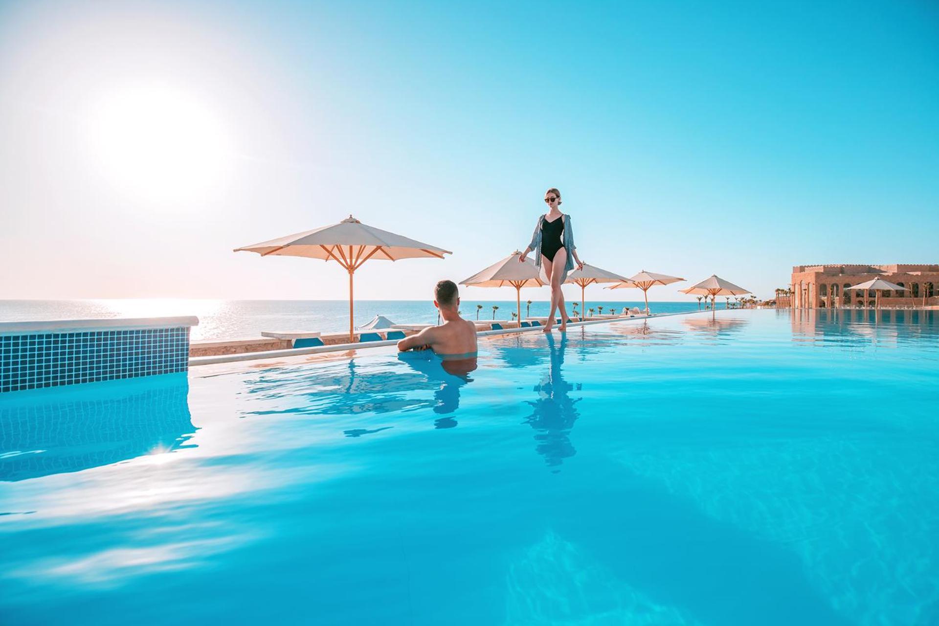 Pickalbatros Citadel Resort Sahl Hasheesh (Adults Only) Hurghada Exterior foto The photo shows a serene pool scene with two people enjoying the water. One person is standing at the edge of the pool, appearing confident and relaxed, while the other is sitting in the water, looking towards the standing figure. The background feat