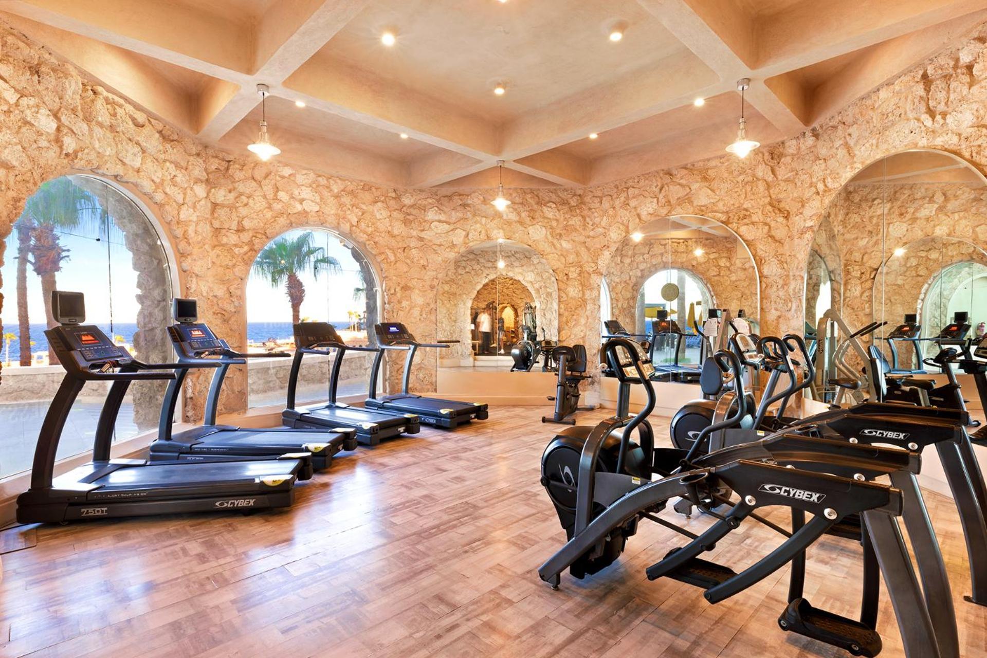 Pickalbatros Citadel Resort Sahl Hasheesh (Adults Only) Hurghada Exterior foto The photo shows a modern gym or fitness area. It features several treadmills lined up in a spacious room with stone walls and arched windows. The flooring is wooden, and there are various exercise machines, including stationary bikes and weight equip