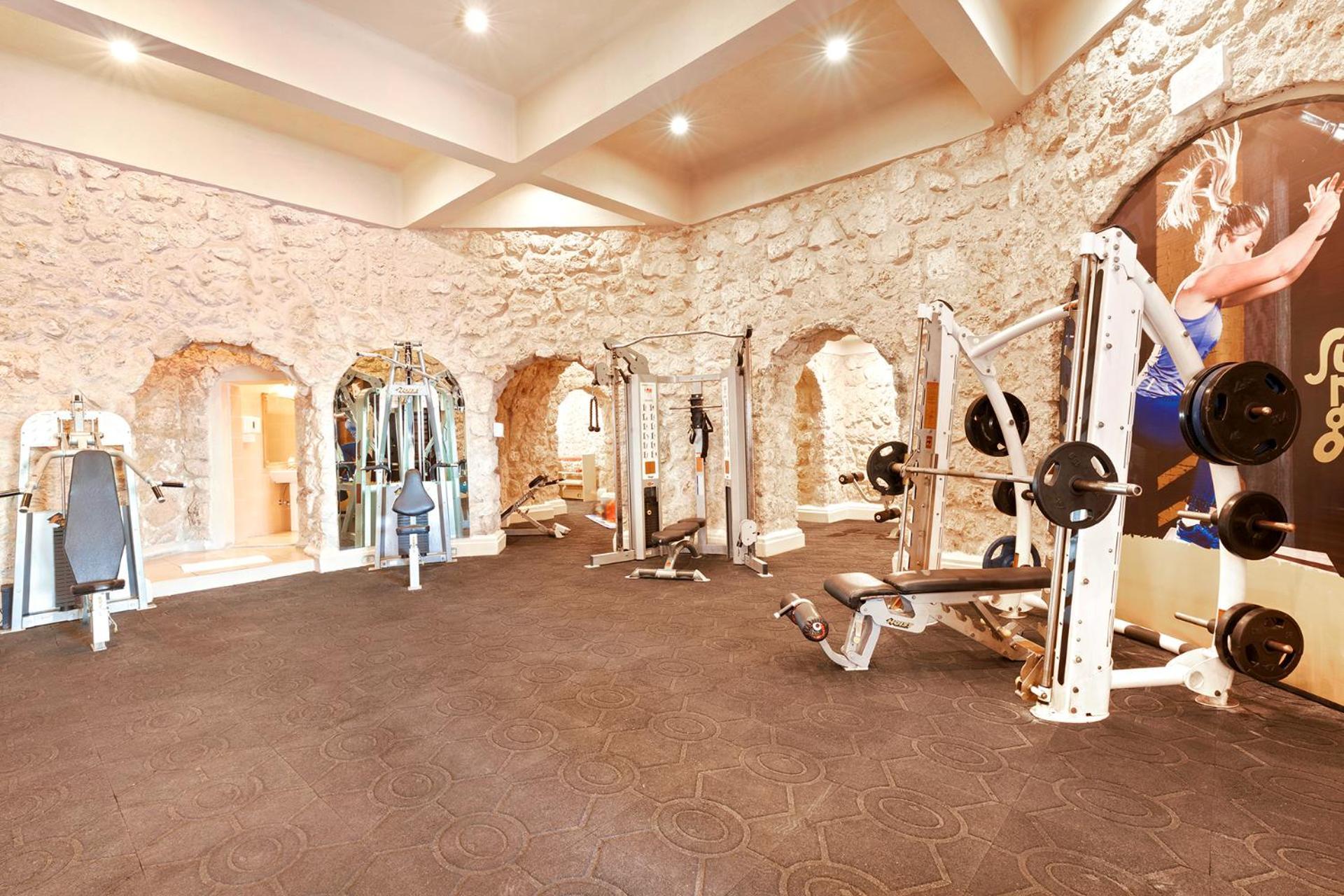 Pickalbatros Citadel Resort Sahl Hasheesh (Adults Only) Hurghada Exterior foto The photo shows an interior of a gym with a unique design featuring stone walls and a spacious layout. The gym is equipped with various exercise machines, including weightlifting equipment and benches. The lighting is bright, and the ceiling is high,