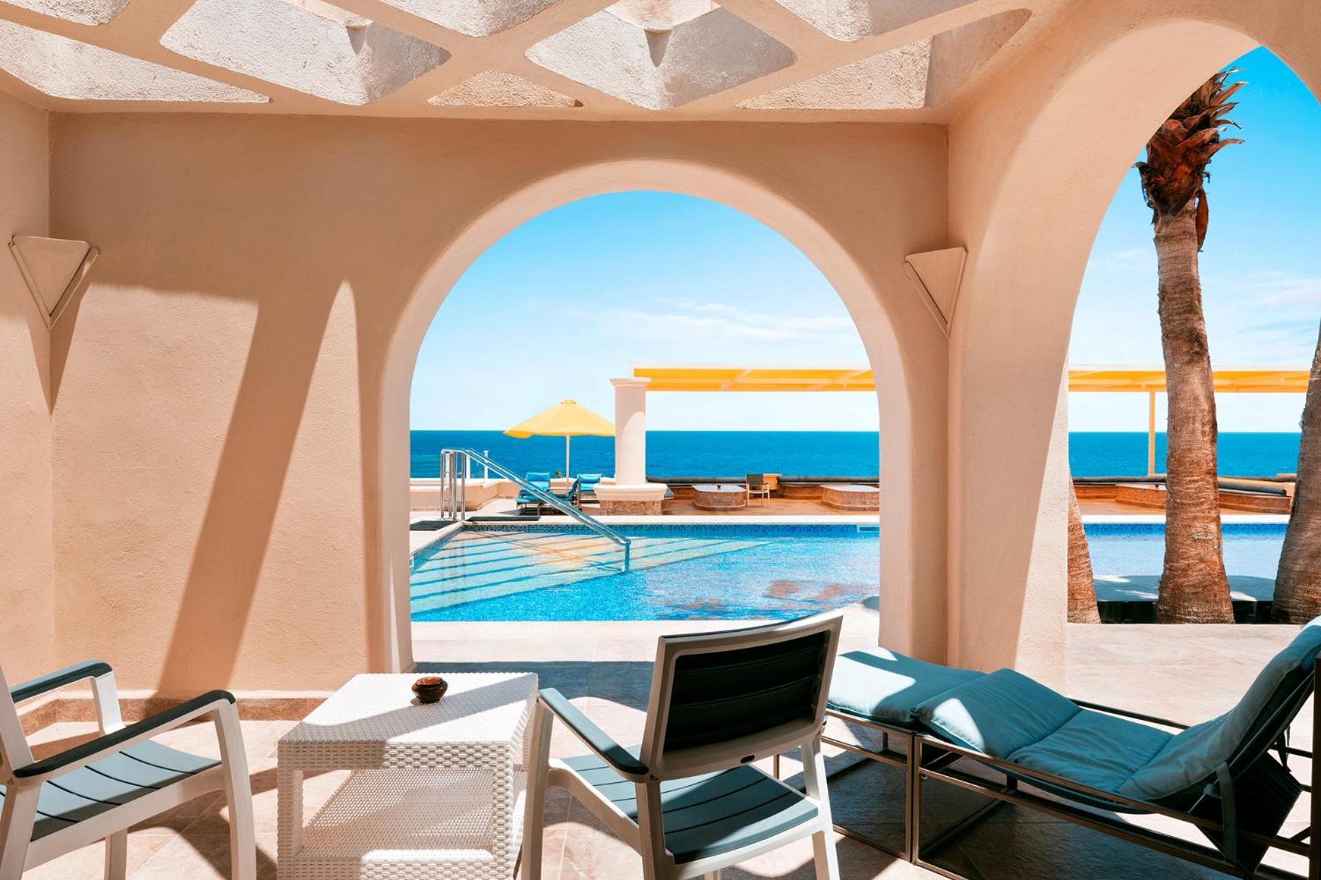 Pickalbatros Citadel Resort Sahl Hasheesh (Adults Only) Hurghada Exterior foto The photo showcases a serene view from a guided archway. In the foreground, there are comfortable lounge chairs arranged near a small table, perfect for relaxation. Beyond the arch, a beautiful pool with a bright yellow umbrella sits adjacent to the 