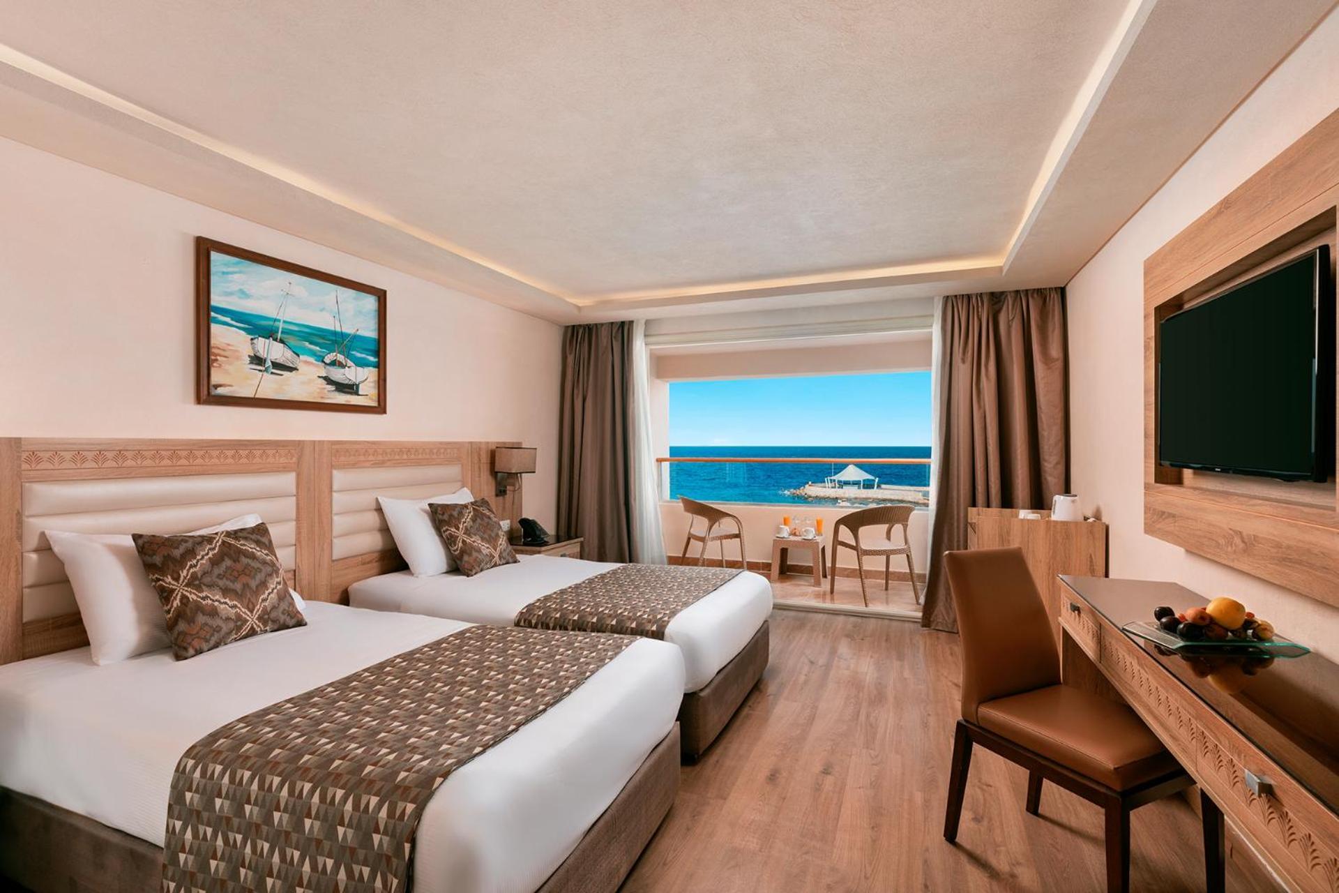 Pickalbatros Citadel Resort Sahl Hasheesh (Adults Only) Hurghada Exterior foto The photo shows a modern hotel room featuring two twin beds with stylish bedding. The room has a large window that offers a view of the sea, and there is a small balcony with outdoor furniture visible. The walls are mostly light-colored, and there’s 