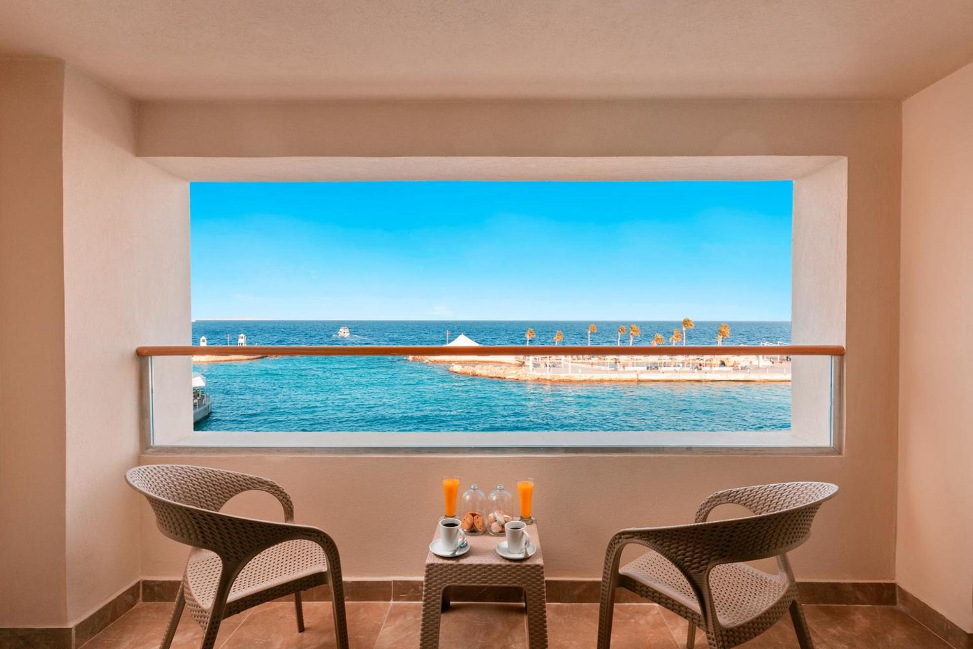 Pickalbatros Citadel Resort Sahl Hasheesh (Adults Only) Hurghada Exterior foto The photo shows a balcony with a stunning view overlooking the ocean. In front of the window, there are two modern chairs made of woven material and a small table between them. On the table, there are two glasses of orange juice and a couple of plate