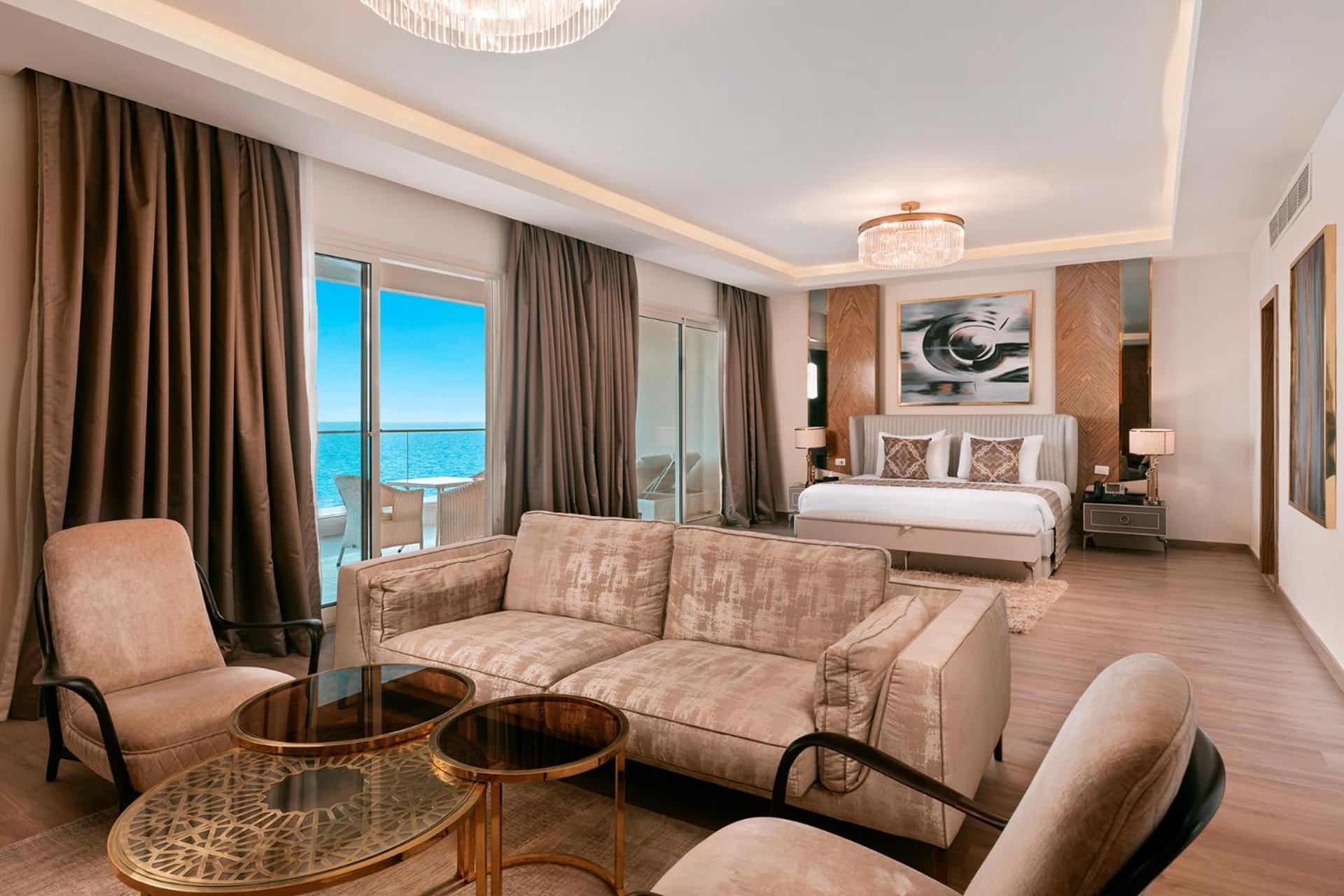 Pickalbatros Citadel Resort Sahl Hasheesh (Adults Only) Hurghada Exterior foto The photo shows an elegantly furnished hotel room or suite. It features a spacious layout with a large bed at the back, adorned with decorative pillows. On one side, there are large glass doors offering a view of the ocean, letting in natural light. 