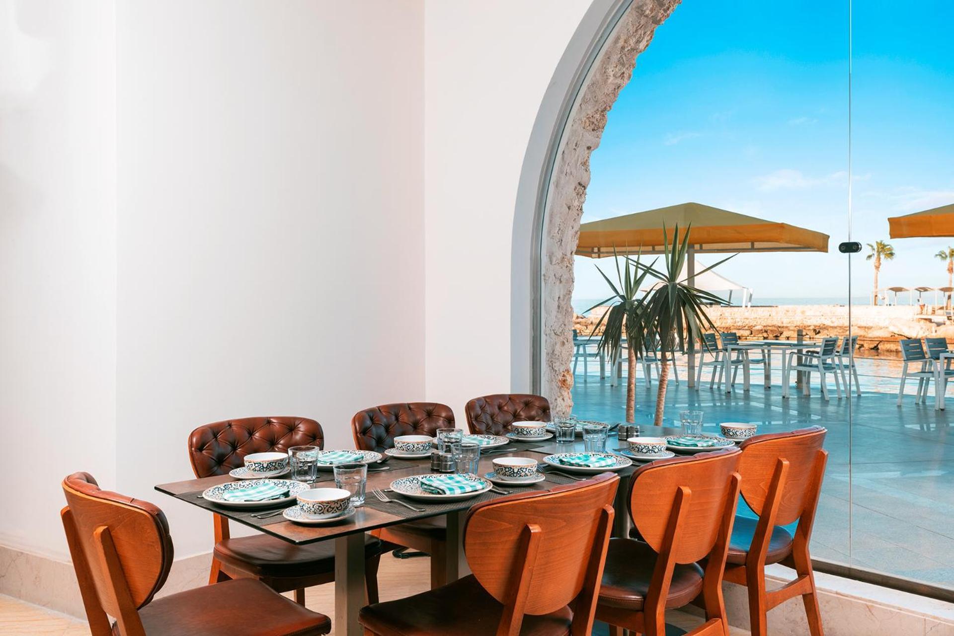 Pickalbatros Citadel Resort Sahl Hasheesh (Adults Only) Hurghada Exterior foto The photo depicts a dining area with a stylish wooden table surrounded by brown upholstered chairs. The table is elegantly set with plates, glasses, and cutlery, suggesting a formal dining setup. In the background, there is a large window or opening 