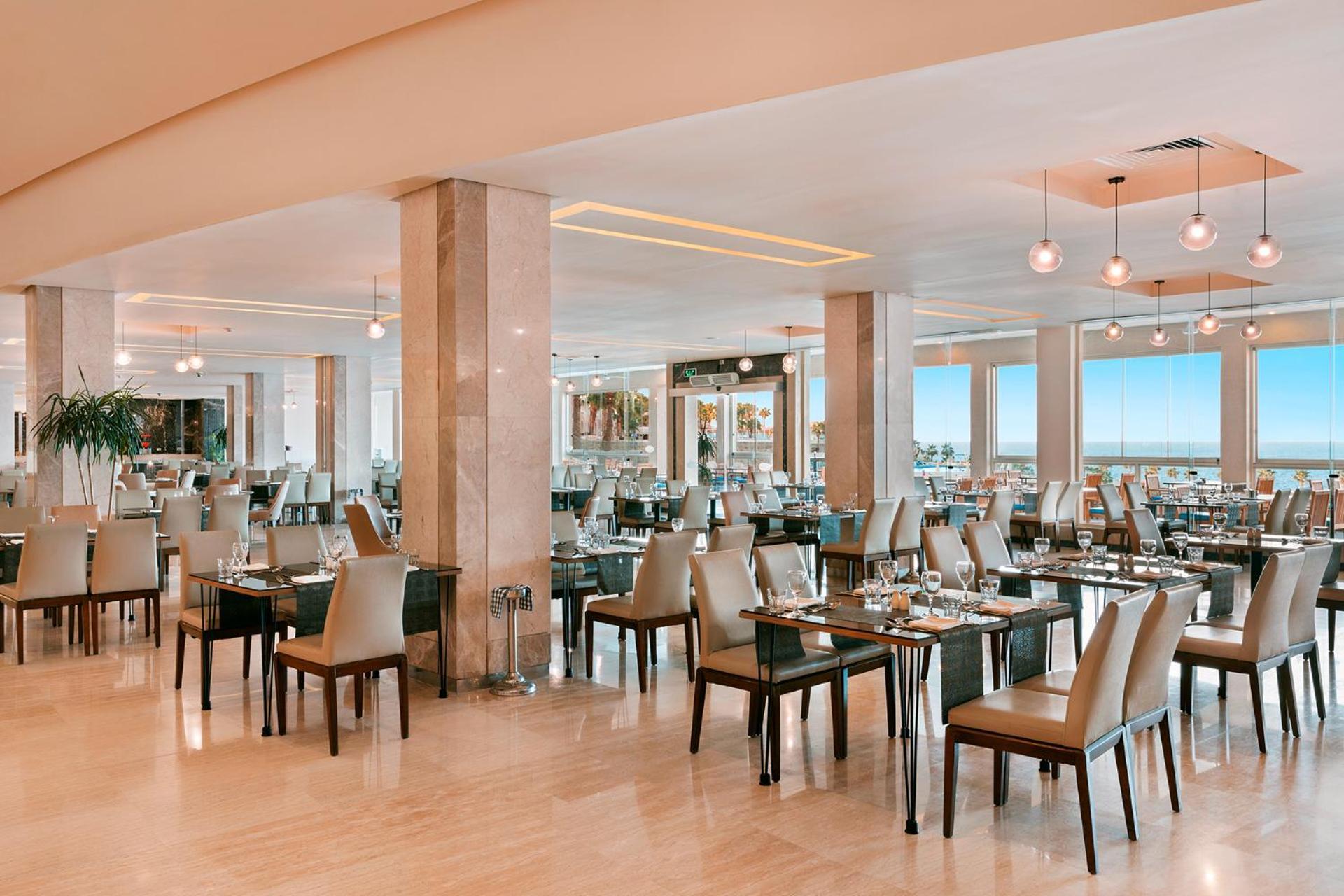 Pickalbatros Citadel Resort Sahl Hasheesh (Adults Only) Hurghada Exterior foto The photo shows a modern and spacious restaurant interior. It features several tables with comfortable chairs arranged in a well-organized layout. The decor includes large windows that provide a view, letting in natural light. The flooring appears to