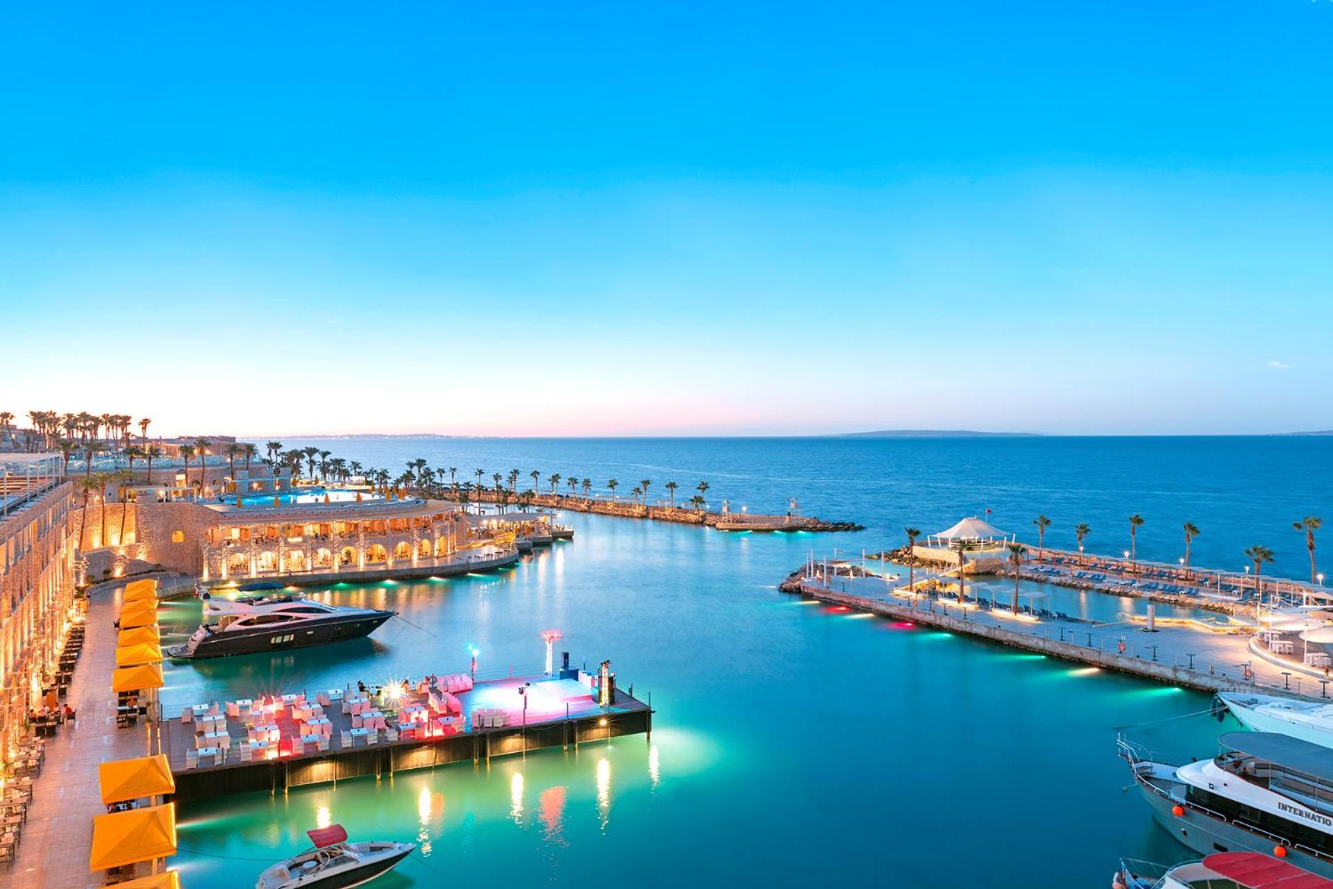 Pickalbatros Citadel Resort Sahl Hasheesh (Adults Only) Hurghada Exterior foto The photo depicts a serene waterfront scene during twilight. There is a marina with several boats and yachts docked at the docks. The water is calm and reflects the colors of the sky, which transitions from blue to shades of purple and pink as the su