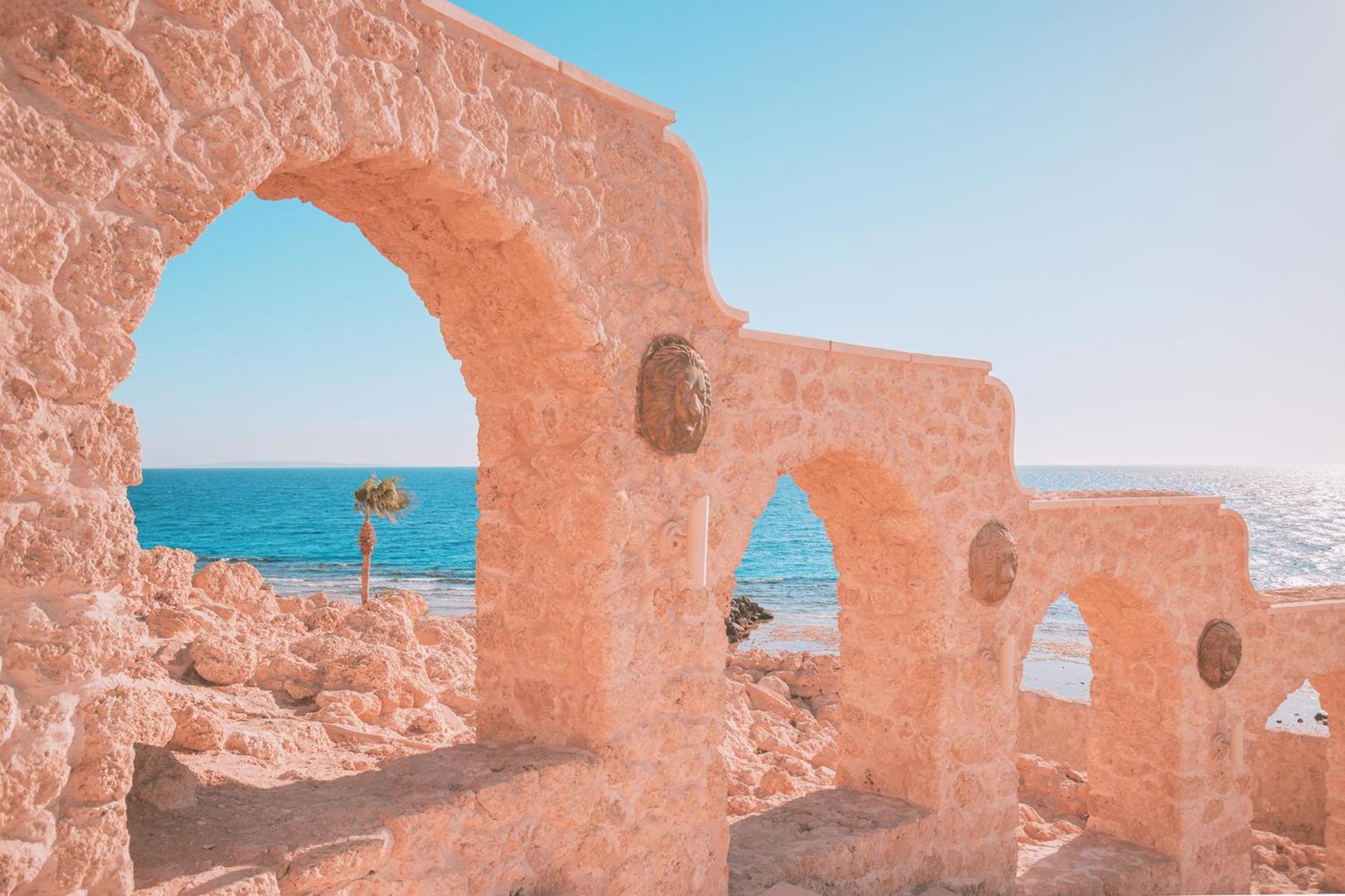 Pickalbatros Citadel Resort Sahl Hasheesh (Adults Only) Hurghada Exterior foto The photo shows a serene coastal scene featuring ancient stone architecture with multiple arches. The walls appear weathered and are made from light-colored stone. Positioned within the arches are ornamental lion heads, adding a decorative touch. In 
