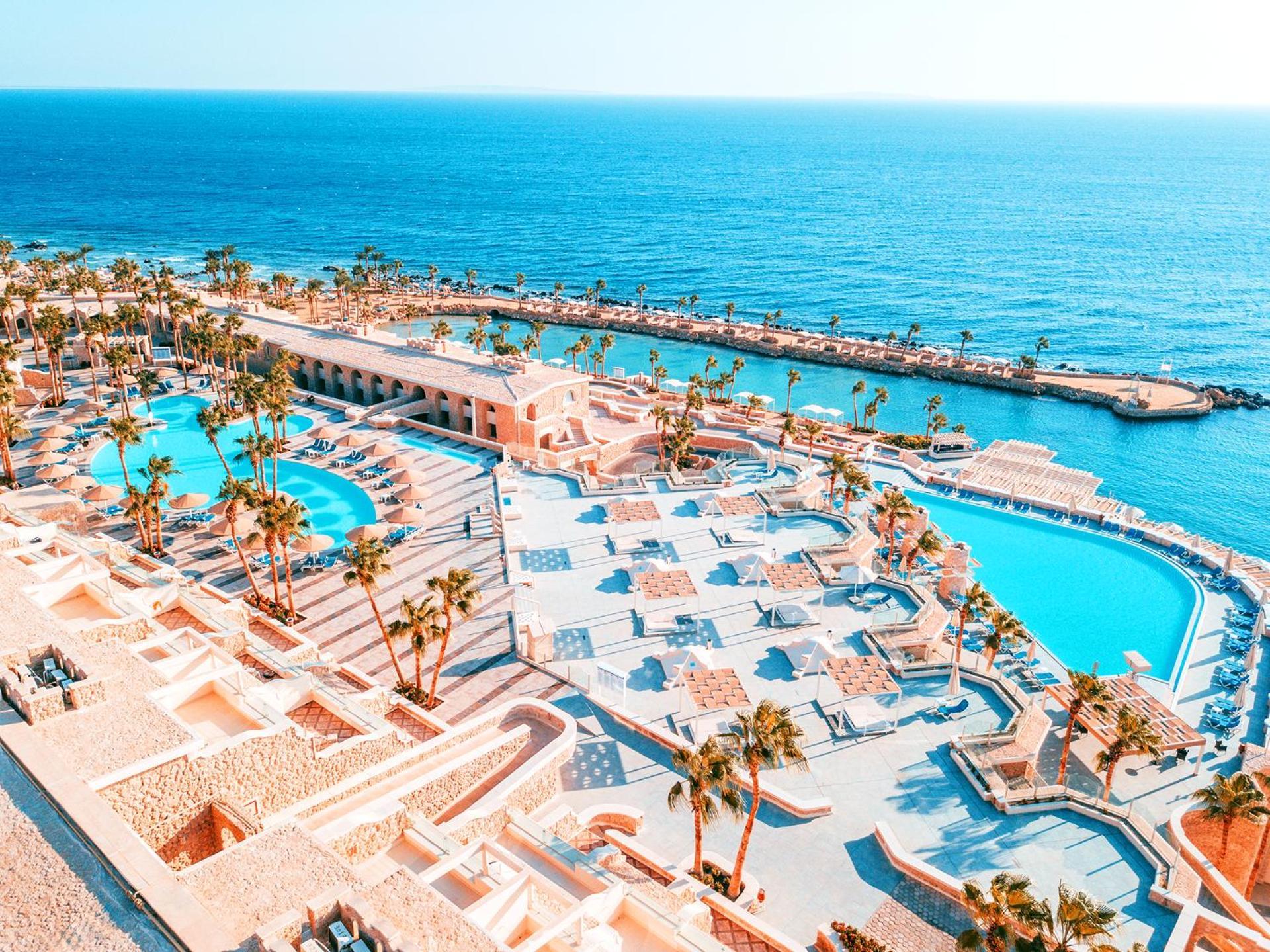 Pickalbatros Citadel Resort Sahl Hasheesh (Adults Only) Hurghada Exterior foto The photo shows a beautiful coastal resort with a stunning view of the ocean. It features multiple swimming pools, surrounded by palm trees and lounge chairs. The design of the resort is spacious and modern, with light-colored buildings creating a re