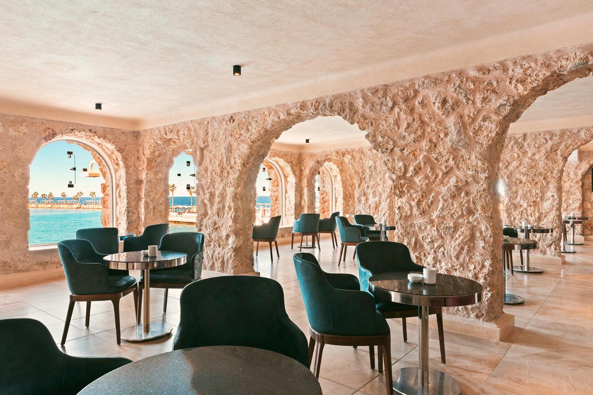 Pickalbatros Citadel Resort Sahl Hasheesh (Adults Only) Hurghada Exterior foto The photo shows the interior of a stylish café or restaurant with a unique architectural design. The walls are made of rough stone, giving a rustic and natural feel. There are several arched openings that provide views of the sea, enhancing the ambia