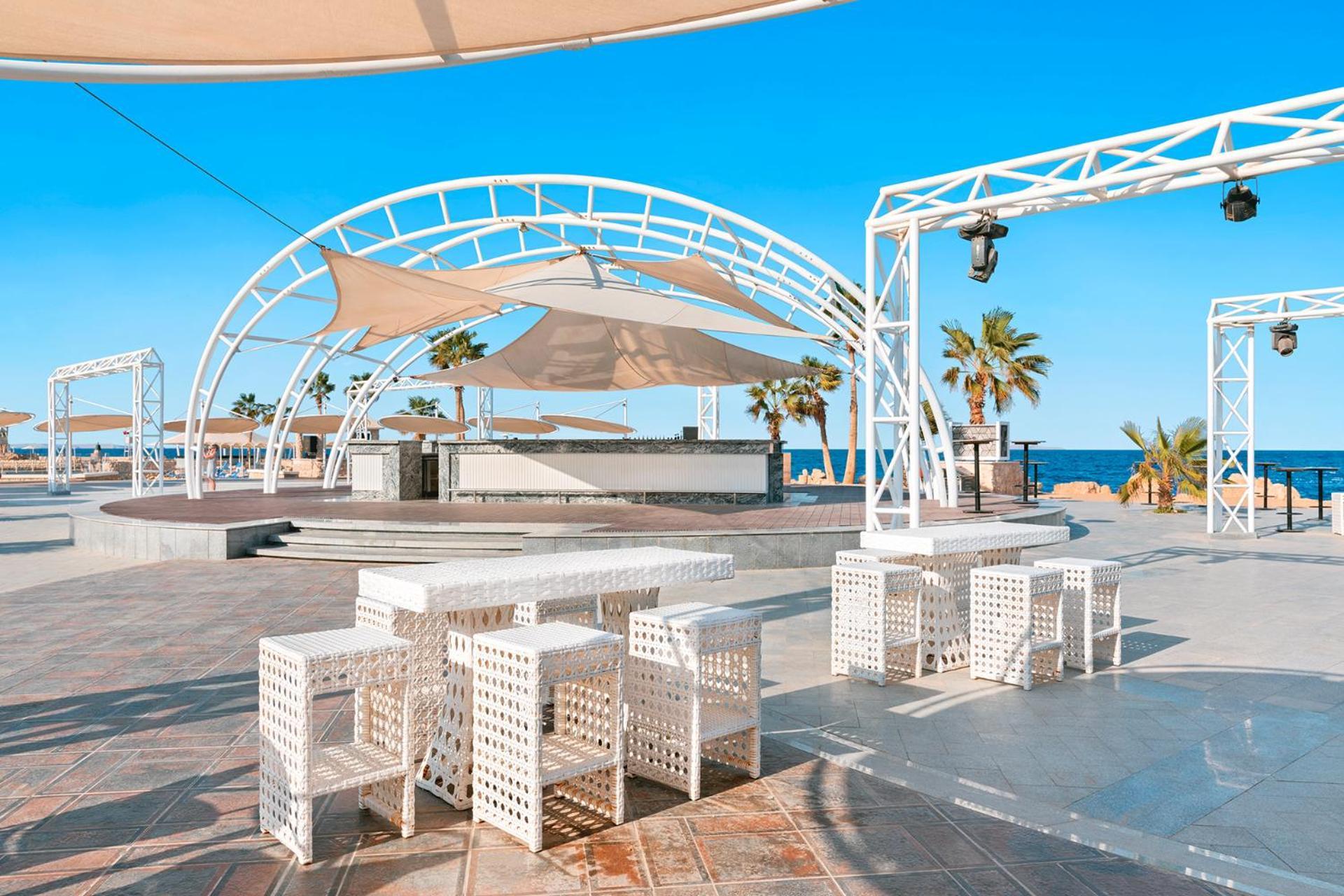 Pickalbatros Citadel Resort Sahl Hasheesh (Adults Only) Hurghada Exterior foto The photo shows an outdoor venue with a modern design, featuring white structures and furniture. There is a large, white canopy providing shade over an area that likely serves as a stage or gathering space. Surrounding the stage are several white, gr